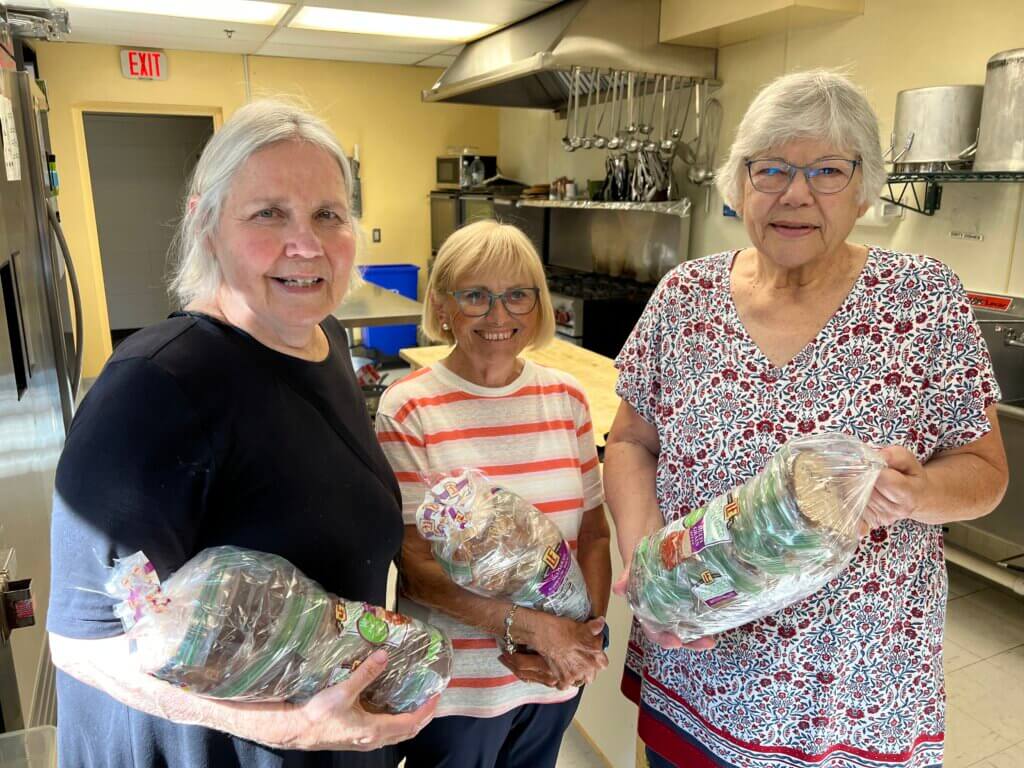 Photo of three members of the Century College Sandwich Squad holding loaves of bread in the church kitchen