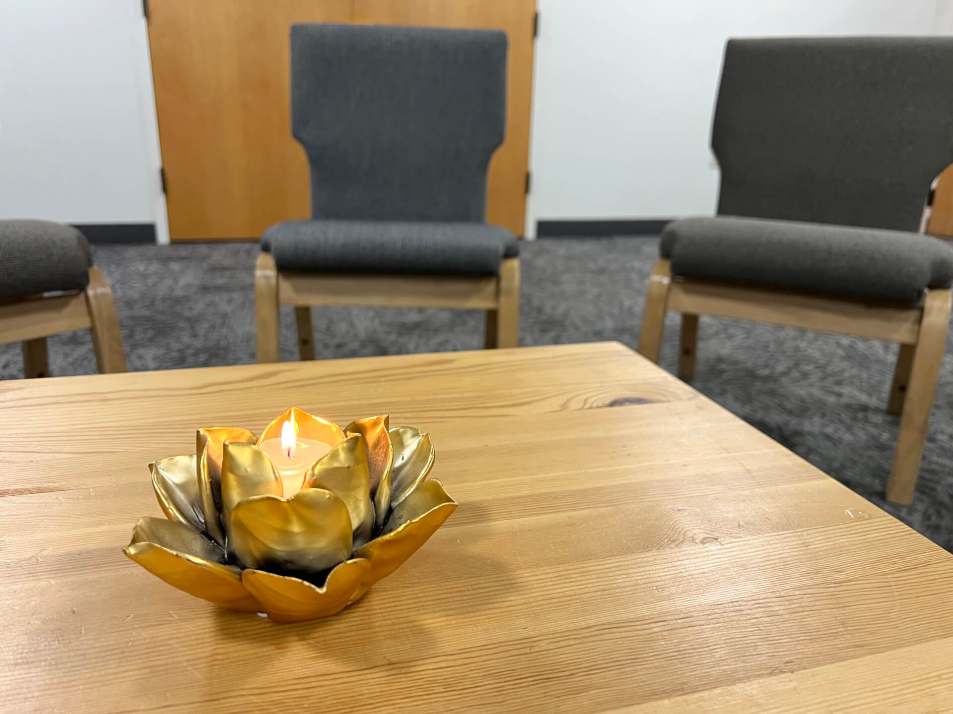 Photo of lit lotus chalice sitting on a wooden table with chairs in the background.